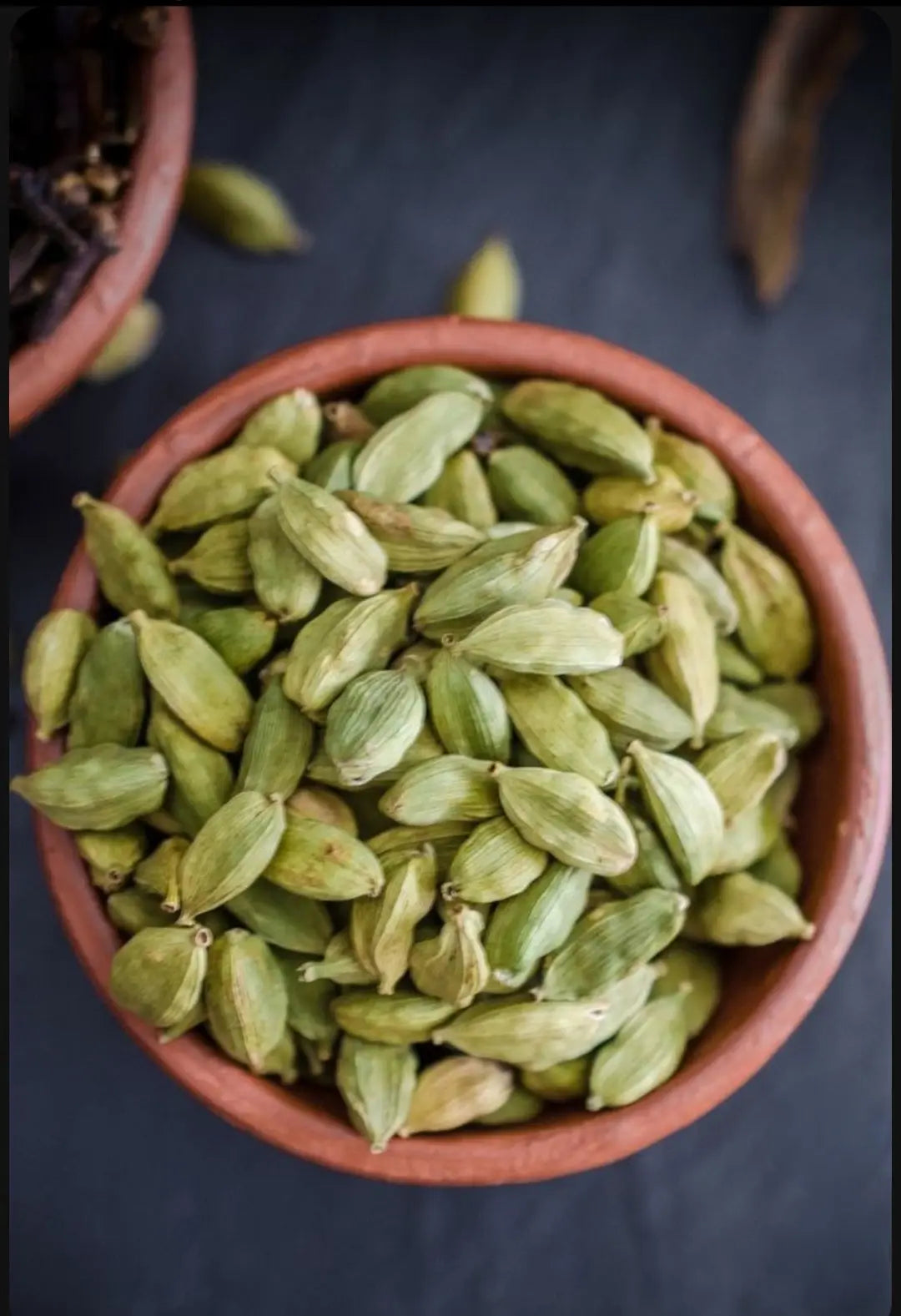 Fresh green cardamom pods in a clay bowl, known for their rich aroma and flavor, perfect for cooking and baking.